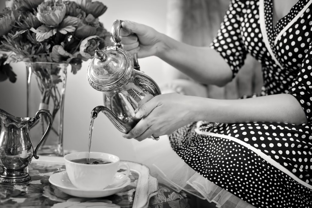 Nainen kaataa teetä mustavalkoisessa vanhanaikaisessa kuvassa